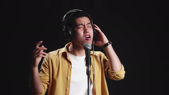 Asian Man Singer Wearing Headphone And Singing Into Microphone On Black Background