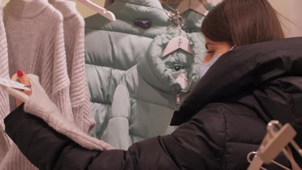 Young Woman in Face Mask Looks at White Pullover Size