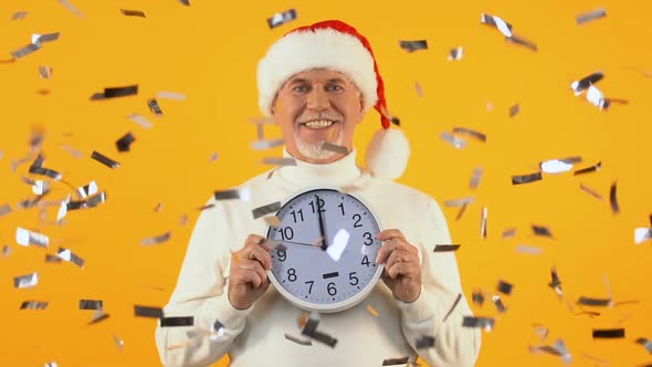 Happy Aged Man in Santa Hat Holding Clock Showing Midnight, New Year Party