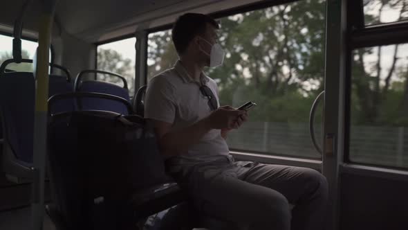Caucasian Man Sits on a Bus at the Window Wearing a Protective Mask Ffp2 Uses a Smartphone in