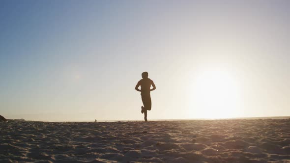 African american man running on beach, exercising outdoors in beach in the evening