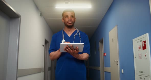 African American Doctor Uses a Tablet Standing in Corridor of Medical Center
