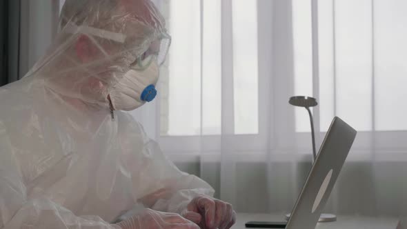 Focused Virologist Wearing Protective Suit Working with Laptop