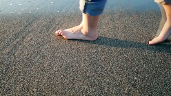 Woman's Legs Leaving Footprint On The Sand Erasing Wave