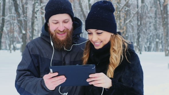 Man And Woman Using a Tablet In The Winter Forest, Smiling. alt