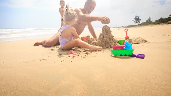 Grandpa Kids Build Sand Castle on Beach by Wave Surf