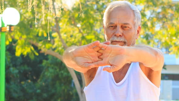 Old Man Does Morning Exercises Stretches Fingers in Park