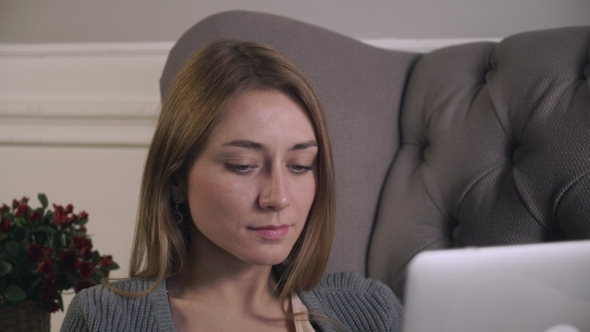 Blonde Woman Works At The Computer Sitting On The Couch