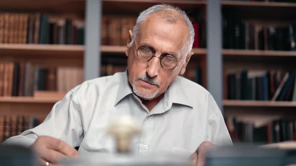 Closeup Elderly Gray Haired Man Reading Book Working at Library Desk Searching Historical Research