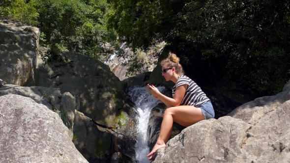 Young Woman Using Tablet Outdoors Sitting Near Waterfall And Smiling.