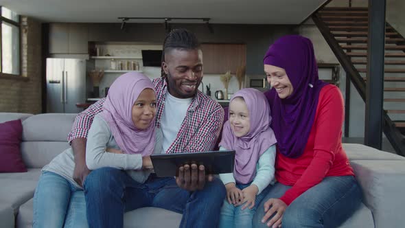 United Multiethnic Muslim Family with Two Adorable Daughters Working Online with Tablet Pc