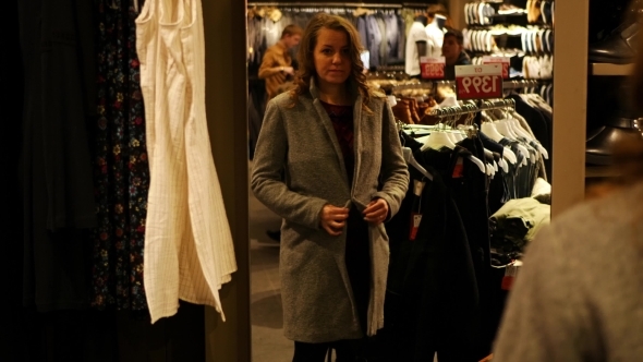 Female In Clothes Shop Fitting On Dress And Looking In Mirror