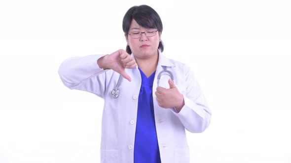 Confused Overweight Asian Woman Doctor Choosing Between Thumbs Up and Thumbs Down