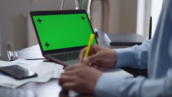 Laptop with Chromakey Green Screen on Table with Male African American Hands Writing Filling in