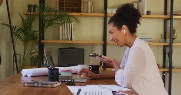 Mixed race woman using laptop and talking on smartphone while working from home