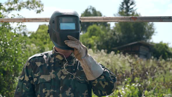 Worker in Camouflage Takes Off Welding Mask at Fence