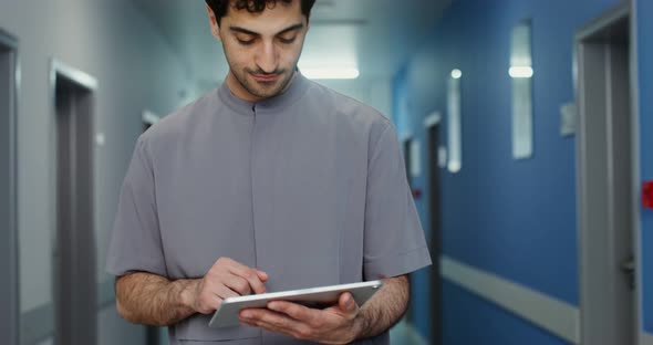 A Doctor Uses a Tablet While Walking Along the Corridor of the Medical Center