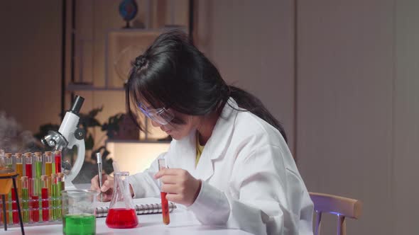 Young Asian Scientist Girl With Dirty Face Mixes Chemicals In Test Tube And Note On Her Book