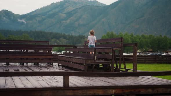 Little Girl Walks Along Wet Wooden Benches on Dancing Ground