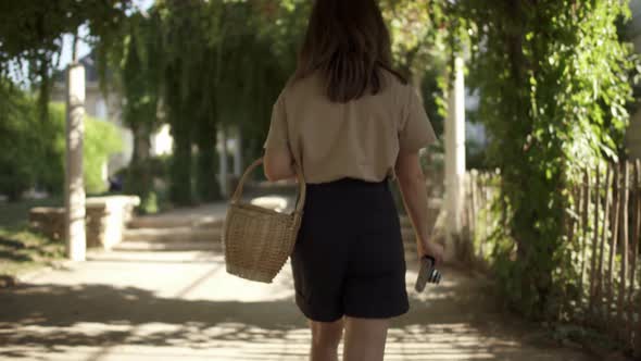 Beautiful Young Woman with Dark Hair Wearing Black Shorts and a Beige Tshirt Is Walking in the Park