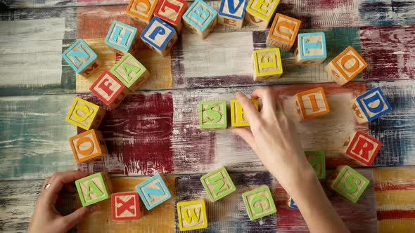 Top View of the Desktop. Women's Hands Add the Word "ASK" From Wooden Cubes