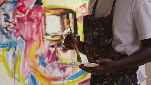 Mid section of african american male artist wearing apron painting on canvas at art studio