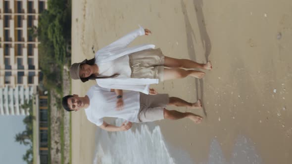 Vertical Video: Young Asian couple in love holding hands and running on the beach cheerful.