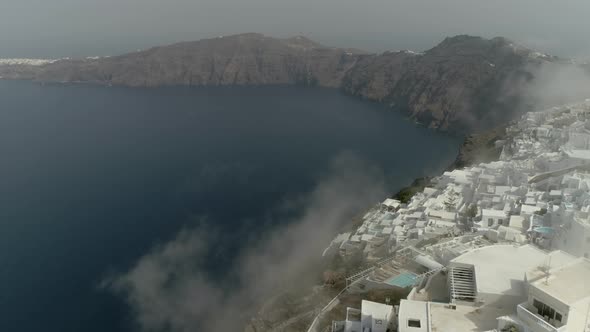 Aerial view over the clouds of traditional white houses on Santorini island.