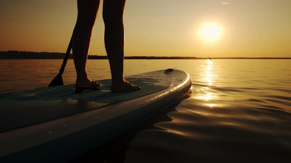 Close Up of Woman Standing Firmly on Inflatable SUP Board and Paddling Through Shining Water Surface