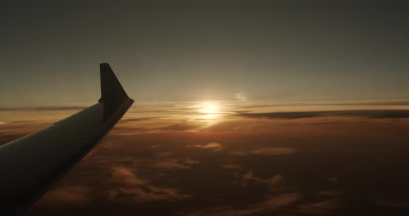 Wing of an Airplane Flying Above the Clouds with Sunset Sky, View From the Window of the Plane