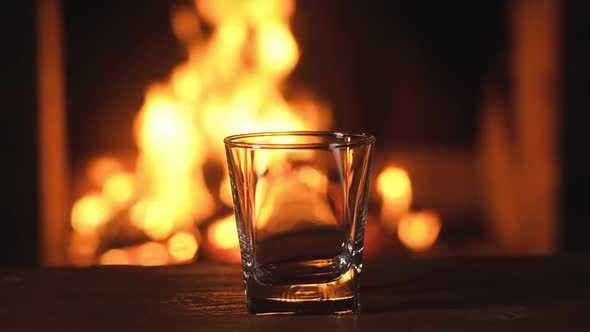 Empty glass for whiskey or brandy is amid the burning flames in the fireplace.