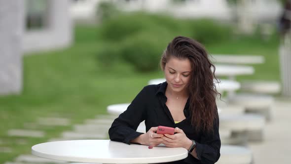 Calm Brunette Woman is Using Smartphone Sitting at Table on Open Terrace Communicating By Online