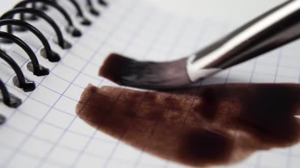 Drawing in brown water paint on a checkered page of a spiral bound school notebook