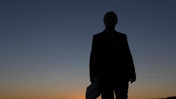 Silhouette of Businessman with Briefcase Walking at Sunset