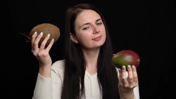 Woman Shows Coconut and Mango in Hands on a Black Background