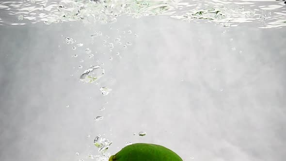 Green Limes Are Thrown Into a Container of Water. Video of Fruit in Slow Motion