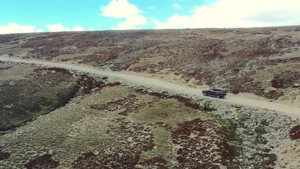 Aerial drone of a red suv driving up a hill slowly on a dirt road path in the high-altitude alpine p