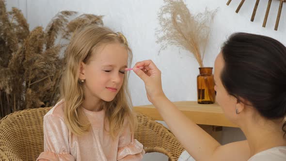 Young Mother Applying Makeup on Daughter Indoors