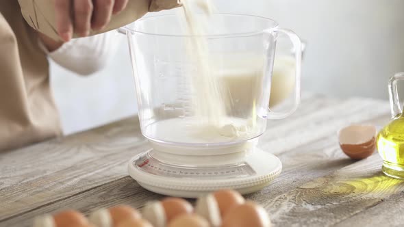 Cook Pours Flour From Craft Bag Into Transparent Measuring Pan Of The Scales. Women Measure Flour