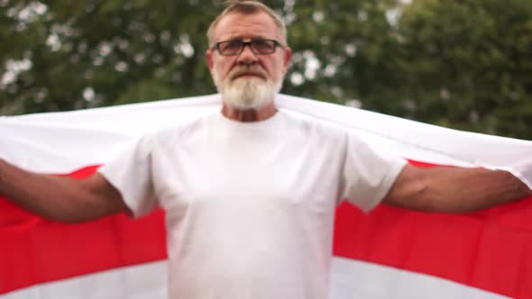 Gray-bearded Mature Man Holds the Flag of Belarus and Stretches It with His Arms in Length Against