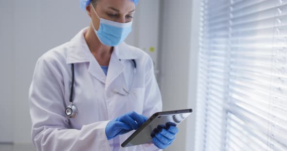 Caucasian female doctor wearing face mask and surgical gloves using tablet