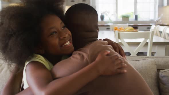 African american daughter and her father smiling and hugging on couch