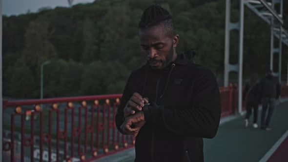 Zoom Out Portrait of Concentrated African American Guy Turning on Activity Tracker on His Smartwatch