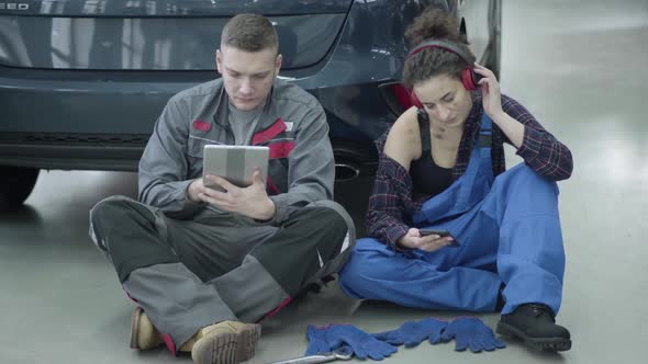 Portrait of Caucasian Man Using Tablet As Young Woman Listening To Music in Headphones. Professional