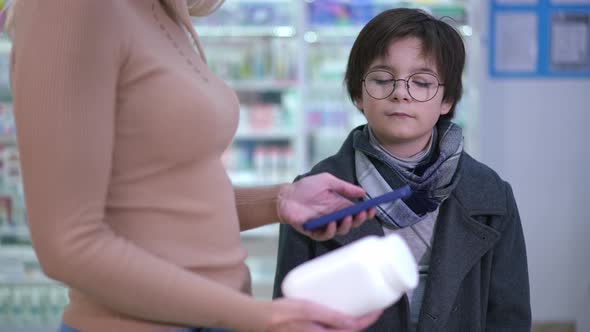 Portrait of Caucasian Boy Standing in Drugstore with Unrecognizable Woman Scanning Pills QR Code
