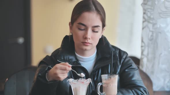 A Girl is Eating Ice Cream in Front of a Cappuccino in a Coffee Shop