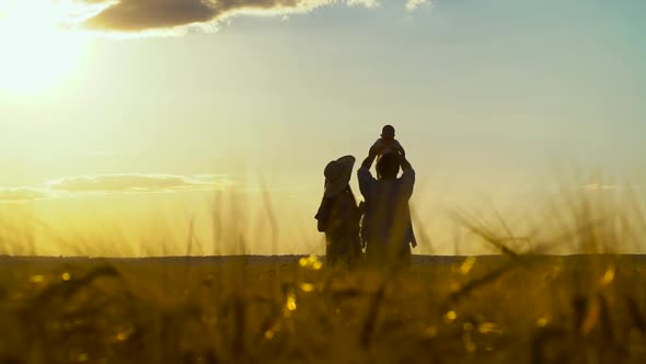 Silhouettes of parents and baby having fun in wheat field at sunset