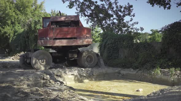 Wide Shot of Abandoned Industrial Truck Standing Over Polluted Paddle in Sunlight. Neglected