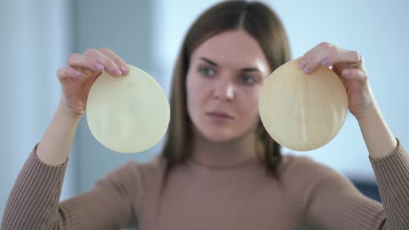Rack Focus From Breast Implants in Female Hands to Thoughtful Caucasian Young Woman Choosing