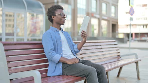 Online Video Chat on Tablet By Young African Man Sitting Outdoor on Bench